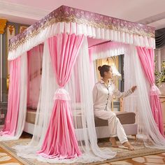 a woman sitting in a pink and white canopy bed