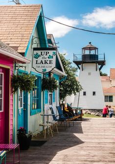 colorful buildings line the boardwalk in front of a white light house with pink trim and blue shutters