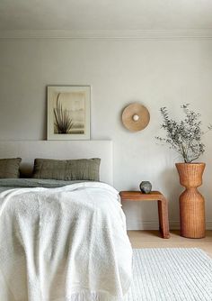 a white bed sitting next to a wooden table with a vase on top of it