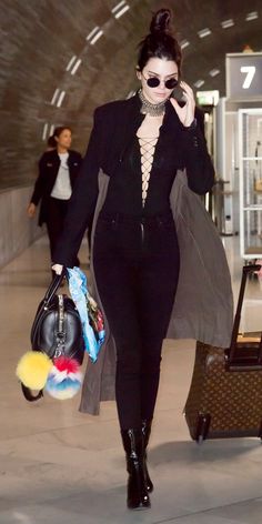 a woman walking through an airport carrying luggage and talking on a cell phone with her handbag