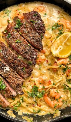 steak, pasta and shrimp in a skillet with lemon wedges on the side