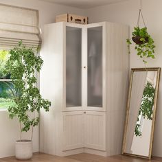 a white cabinet sitting next to a mirror and potted plant on top of a wooden floor