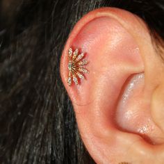 a woman's ear is adorned with an intricate gold and white diamond starburst