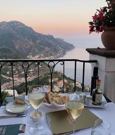 two glasses of wine are sitting on a table overlooking the ocean and mountains in italy