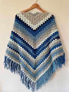 a blue and white crocheted ponchle hanging on a wooden hanger