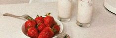 strawberries in a bowl on a white table with silverware and utensils