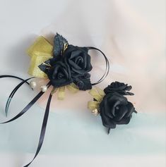 two black flowers with gold accents on a white cloth background, one is tied to a ribbon and the other is made out of fabric