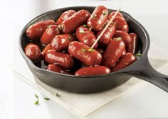 a skillet filled with hot dogs on top of a white cloth next to a fork