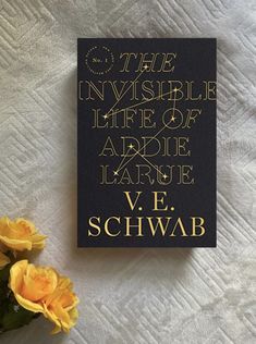 there is a book with gold lettering on it and yellow flowers in the foreground