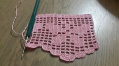 a pink crocheted doily sitting on top of a wooden table next to a green knitting needle