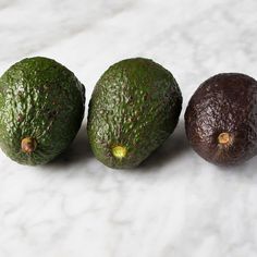 three avocados sitting next to each other on a white counter top in front of one another