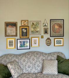 a living room filled with lots of framed pictures on the wall and couches covered in pillows