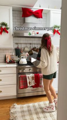 a woman standing in front of an oven with christmas decorations on the wall and stockings hanging from it