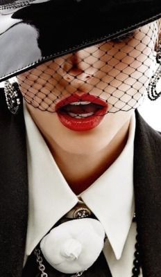 a woman wearing a black hat with a veil over her head and red lips,