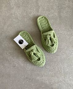 a pair of green crocheted slippers with tassels on the toes