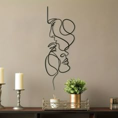 a metal sculpture on the wall next to a table with two candles and a potted plant