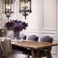 a dining room table and chairs with chandeliers hanging from the ceiling above it