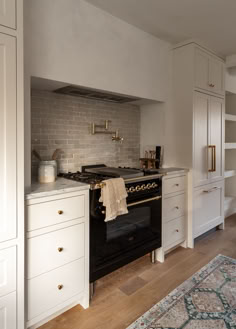 a kitchen with white cabinets and an oven in the center, along with a rug on the floor