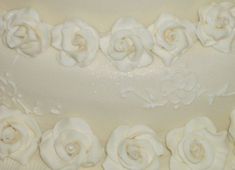 a close up view of a wedding cake with white frosting roses