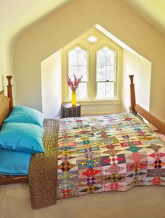 a bed with a quilt on top of it in a bedroom next to a window