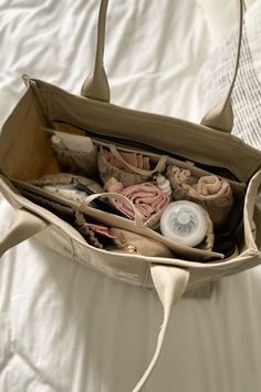 a purse filled with lots of items on top of a white bed covered in sheets