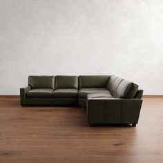 a green leather couch sitting on top of a wooden floor next to a white wall