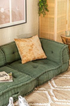 a green couch sitting in front of a window next to a wooden table with two pairs of shoes on it