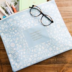 a book with glasses on top of it next to pens and pencils in a bag