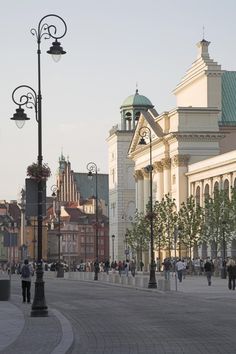 people are walking down the street in front of some tall buildings and lamps on poles