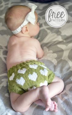 a baby laying on top of a bed wearing a green diaper with white hearts