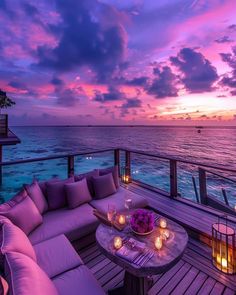 a couch and table on a deck overlooking the ocean at sunset with candles lit up