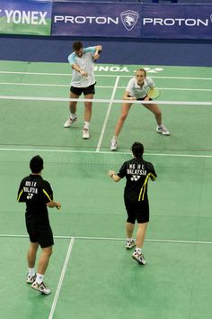 three people playing tennis on a green court