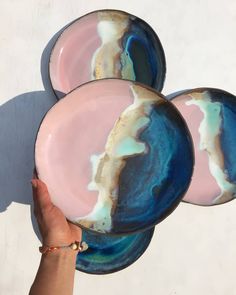 three plates with blue, pink and gold designs on them are being held by a woman's hand