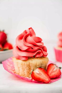 a cupcake with pink frosting and two strawberries on the plate next to it