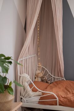 a white bed sitting under a canopy next to a plant in a room with striped walls