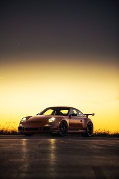 a car is parked on the side of the road in front of an orange and yellow sky