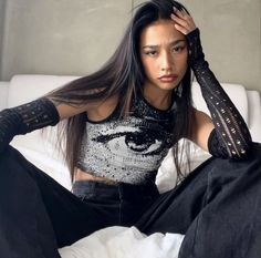 a woman sitting on top of a white bed wearing black gloves and holding her hair