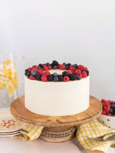 a white cake topped with berries and blueberries on top of a wooden platter