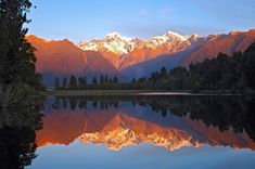 a mountain range is reflected in the still water of a lake with trees on both sides