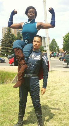 a man and woman dressed as captain america standing in the grass near a street sign