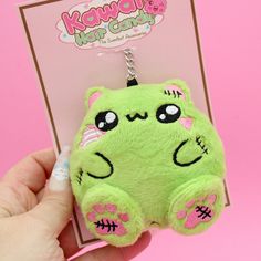 a green stuffed animal keychain with pink eyes and fangs on it's face