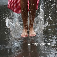 a person standing in the water splashing with their bare feet and red checkered dress