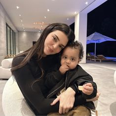 a woman holding a small child in her lap while sitting on a white couch with an open floor plan