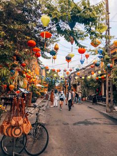 people walking down the street with many colorful lanterns hanging from the ceiling above them and bikes parked on the side of the road