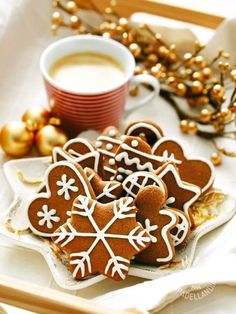 gingerbread cookies with icing on a plate next to a cup of coffee and gold ornaments