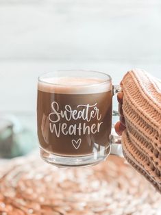 a person holding a coffee mug with the words sweater weather written on it