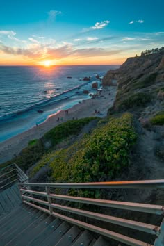 the sun is setting over the beach as people walk up stairs