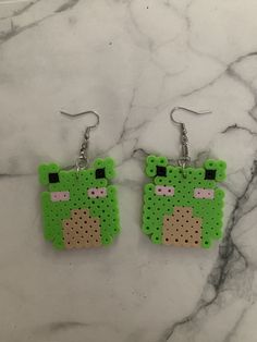 a pair of earrings made out of perler beads with a green bear on it