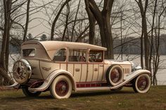 an old fashioned car parked in front of some trees near the water's edge