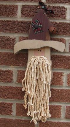 a wooden mask with dreadlocks and a hat on it hanging from a brick wall